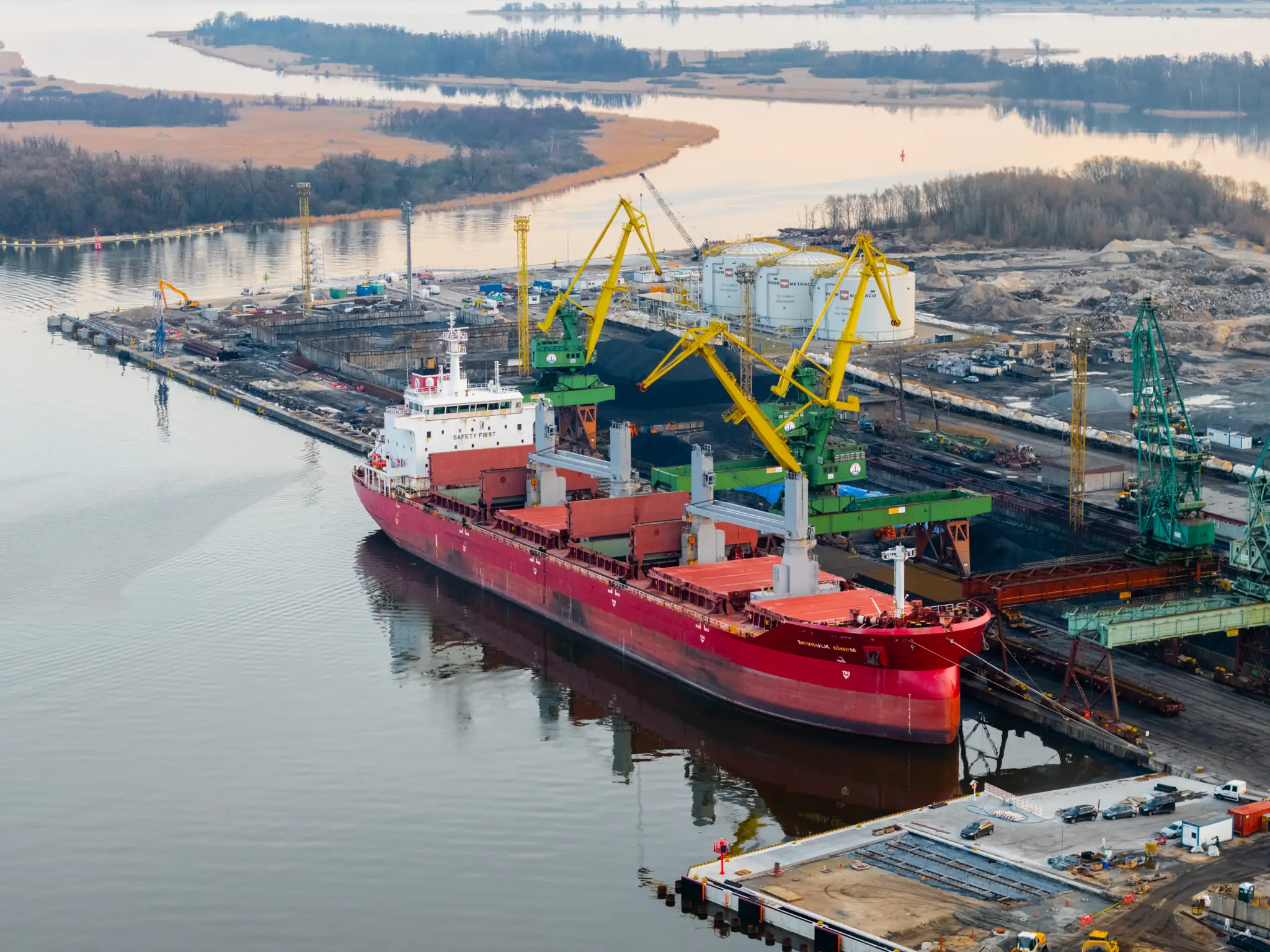 A modern dry bulk vessel alongside a cargo terminal, loading equipment and cargo handling visible.